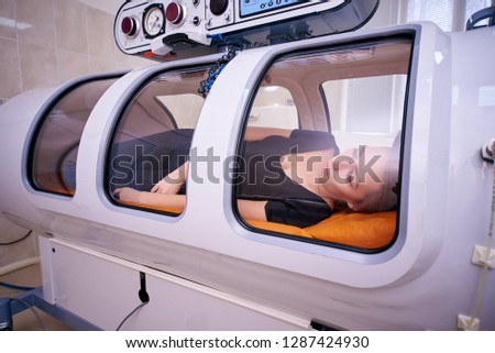 a girl in a black T-shirt lies in a hyperbaric chamber, oxygen therapy, a medical room Royalty-Free Stock Photo #1287424930