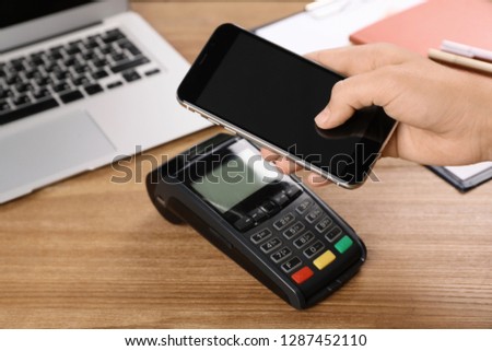 Woman using terminal for contactless payment with smartphone at table