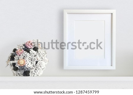 Empty wooden frame next to a floral decoration bouquet on a shelf. Art or portrait mock up and empty copy space for Editor's text.