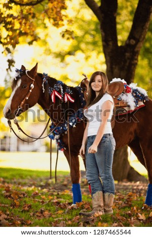 Teenage girl stands by her horse which is decorated with tinsel and American flags.
