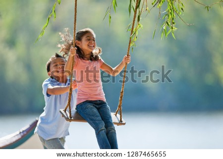 Happy young boy pushing a young girl on a tree swing. Royalty-Free Stock Photo #1287465655