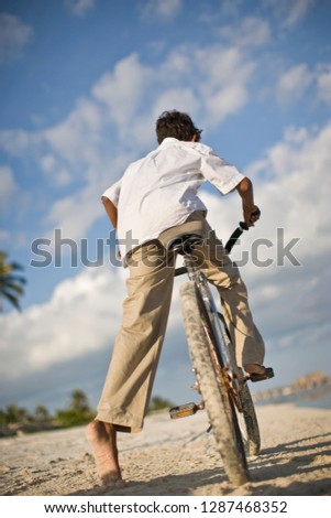 Boy riding a bicycle along a beach.