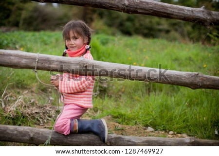 Portrait of a young girl looking through a log fence on a farm.