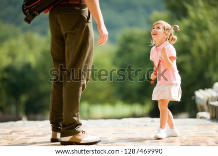 Young girl standing with her father playing with a golf club.