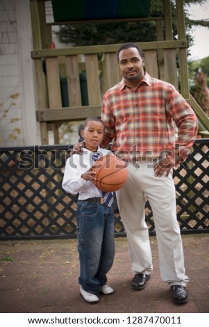 Portrait of a young boy holding a basketball while standing next to his father.