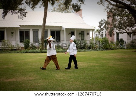 Young adult male chef walking behind a mid-adult man carrying room service.