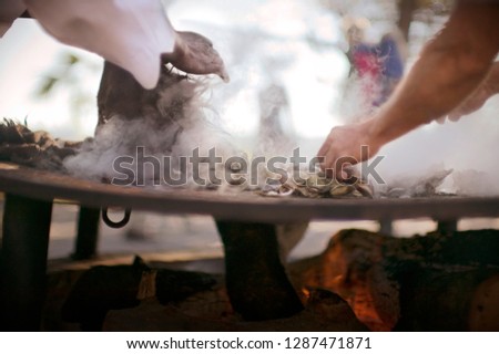Hands of men picking up oysters that are cooking over coals.