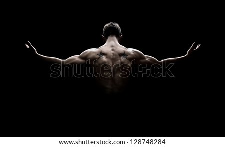 Rear view of healthy muscular young man with his arms stretched out isolated on black background Royalty-Free Stock Photo #128748284