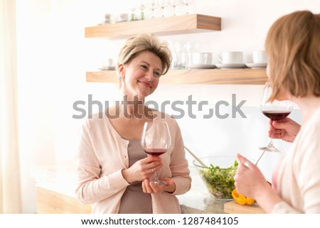 Smiling mature women holding wineglasses while standing in kitchen