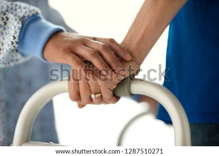 Nurse lays a supporting and comforting hand atop a young male patient's hand as he learns to walk again.