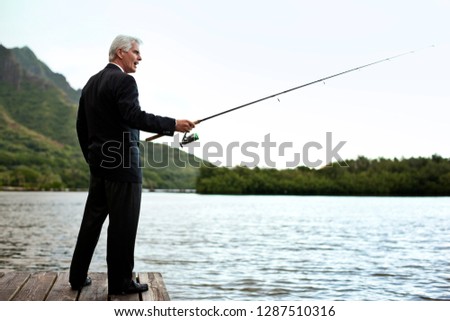 Formally dressed mature businessman fishing on the lake.