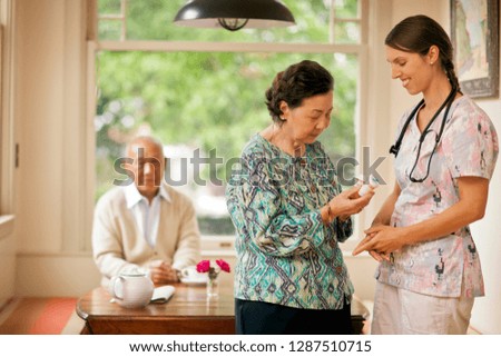 Smiling nurse giving a senior woman pill bottles.