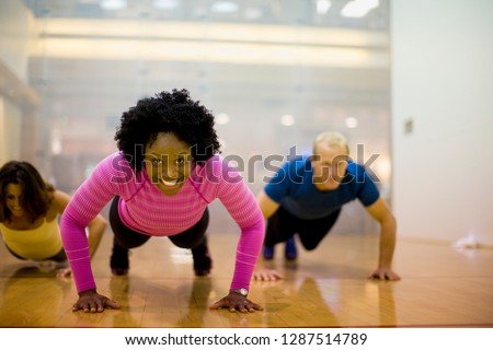 Portrait of a smiling young woman doing press ups inside a gym.