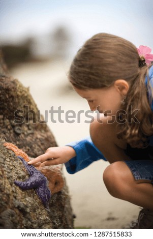 young girl touches starfish on a rock