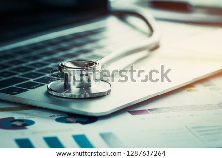 Stethoscope on computer with test results in Doctor consulting room background and report chart for medical costs in modern hospital on Laptop desk. Healthcare costs business, fees concept. Gray tone Royalty-Free Stock Photo #1287637264