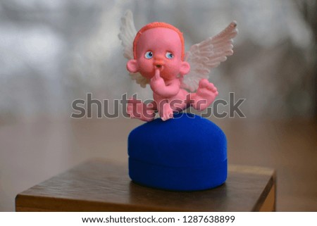 a small figure of an angel sitting on or near a blue jewelry box close up