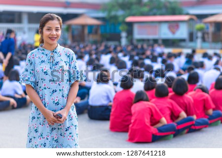 A female high school teacher is standing among students, Thailand, southeast Asia.