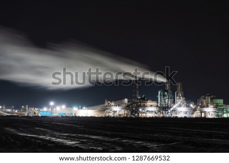 Industrial factory on a night background, with a lot of pipes from which there is a lot of smoke.
