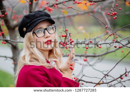Cute young woman in glasses and cap, in a red coat walking in the park in the fall of the year.
