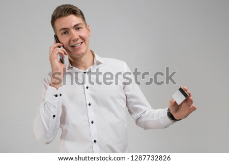 Portrait of young man talking on mobile phone with credit card in hand isolated on white background