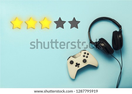 Gamepad and headphones on a blue background. Added a rating of three stars. Reputation. The concept of the game on the console, gambling. Flat lay, top view.