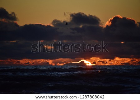 Storm on the sea at sunset. Blue sky with dark clouds. The light of the sun on the horizon. Big waves roll ashore.