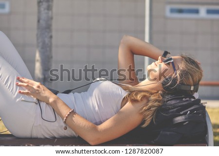 Young woman in a white T-shirt with listening music and lies on the pavement