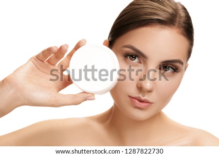Cute girl preparing to start her day. She is applying moisturizer cream on face at studio. The beauty, care, skin, treatment, health, spa, cosmetic and advertising concept