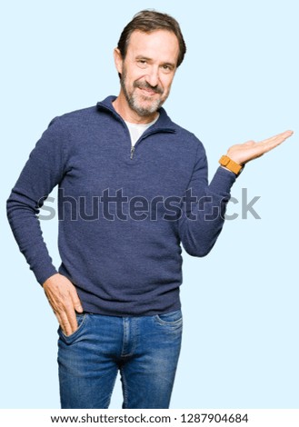 Middle age handsome man wearing a sweater smiling cheerful presenting and pointing with palm of hand looking at the camera.