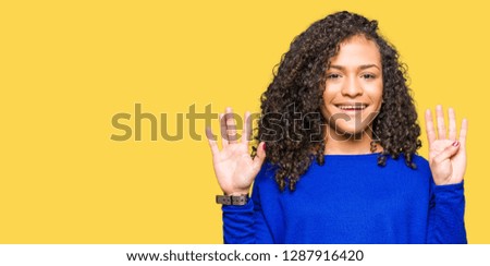 Young beautiful woman with curly hair wearing winter sweater showing and pointing up with fingers number nine while smiling confident and happy.