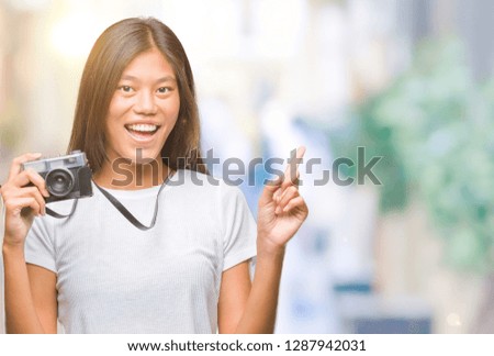 Young asian woman holding vintagera photo camera over isolated background surprised with an idea or question pointing finger with happy face, number one