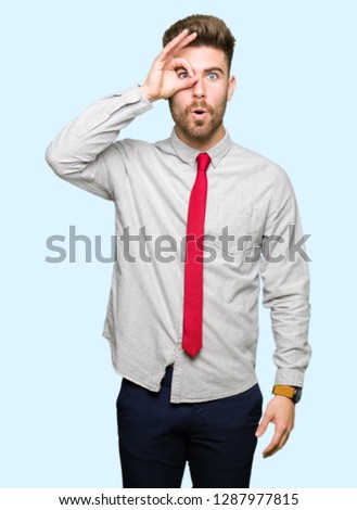Young handsome business man doing ok gesture shocked with surprised face, eye looking through fingers. Unbelieving expression.