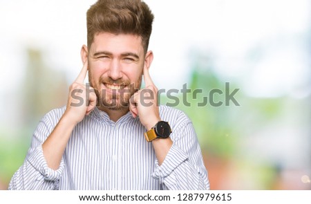 Young handsome man covering ears with fingers with annoyed expression for the noise of loud music. Deaf concept.