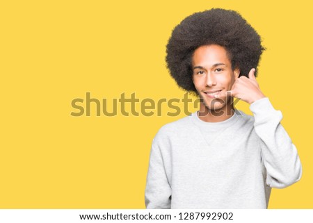 Young african american man with afro hair wearing sporty sweatshirt smiling doing phone gesture with hand and fingers like talking on the telephone. Communicating concepts.