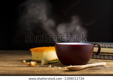 There is a book of bread and a cup of coffee with hot smoke, with the aroma of coffee placed on an old wooden table. Simple work area or coffee break in the morning
