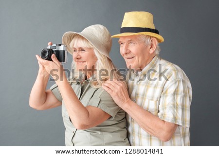 Senior couple tourists wearing beach hats studio standing isolated on gray husband hugging wife holding camera taking pictures smiling happy