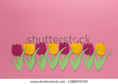 Red and yellow tulips of paper on pink background, one line 