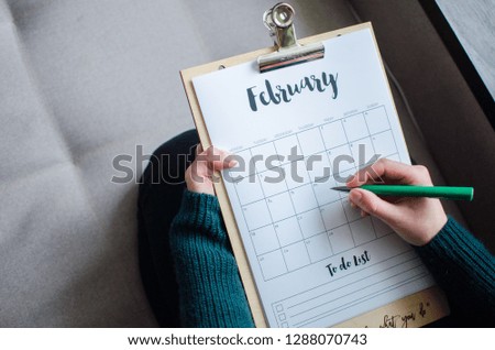 Top view of women hands writing goal for February month  on opened blank calendar.  Copy space. Flat lay. 