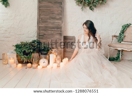 A girl in a beige peignoir, with a wreath of flowers on her head, poses in the studio loft, fine art wedding style