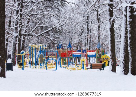 Empty colorful kids playground on yard in the park in cold snowly winter