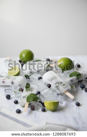 Lemonade Ice Lollies grouped together on a bed of ice with blueberries and mint. 