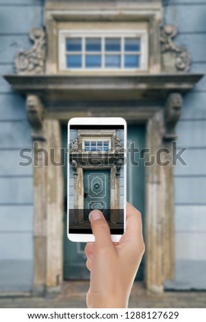 A man is making a photo of old blue door with beautiful columns, a visor and a window. Old town, Riga, Latvia on a mobile phone