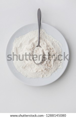 White powder in silver spoon over white background. Top view. Detailed close-up shot. Icing, caster, confectioners or powdere sugar pile. Flour flat lay.
