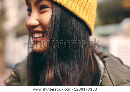 Close up of a smiling woman in winter clothes standing outdoors. Cropped shot of a smiling asian woman in winter cap standing outdoors.