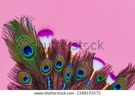 Cosmetic Makeup Brush Set and Colorful peacock feathers on pink background, copy space, text place. Cosmetics Professional Make up fashion background, flat lay