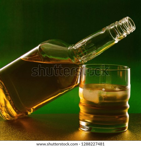 Bottle and glass with whiskey on a green golden background.