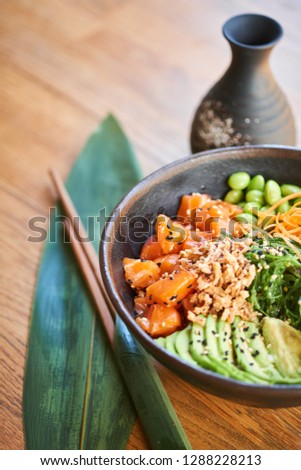 Close-up of poke bowl and chopsticks on wooden background. Traditional Hawaiian and Japanese cuisine.