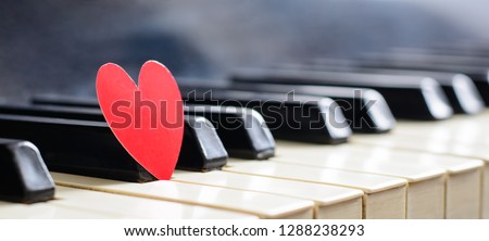 Long panoramic photo of small red heart on piano keyboard. Concept of love, valentine's day