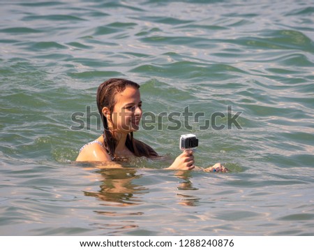 Girl holding action camera in waterproof case. Compact gadget waterproof, support 4k video, voice controls and is often used in extreme photography