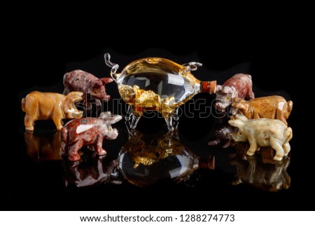 Pig figurines made of onyx, jasper, glass, gold on a black background close up